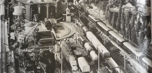 Ein schicker Verkaufsraum der 60er Jahre mit prall gefüllten Regalen und Vitrinen. Doch was macht man mit der letzten verbliebenen kahlen Wand? Ganz einfach: man bestellte bei Märklin die “Dekoration-Groß-Fotos”. Aus dicker Pappe und schwarz...
